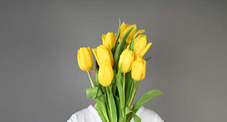Girl holding a bouquet of yellow tulips on gray bacckround with copy space. High quality photoの写真素材