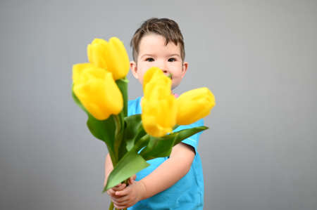 Cute little boy holding a bouquet in front of his face on a gray background. High quality photoの写真素材