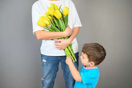 Small son gives his mother a bouquet of beautiful tulips on gray background. High quality photoの写真素材