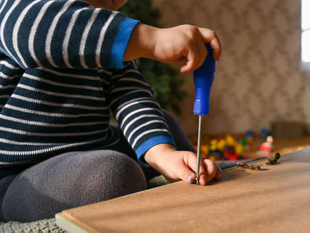 A small boy unscrews the screws with a screwdriver. Boy plays with screwdriver at home, close up....