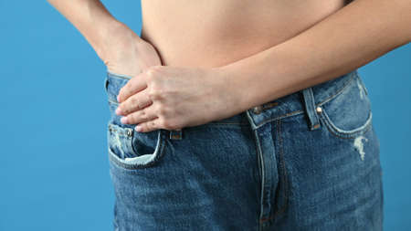 Woman shows that she has lost weight and her old jeans got too large, blue background with copy space. High quality photoの写真素材