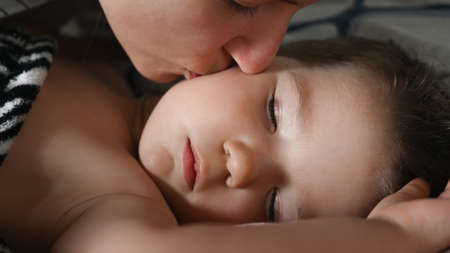 The mother gently kisses the sleeping son, the little boy does not want to wake up. High quality photoの写真素材