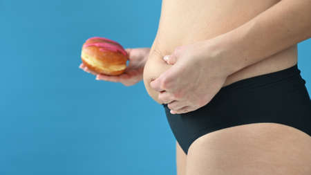 A woman in underwear holds a donut in her hands and touches her fat stomach, a diet concept. High quality photoの写真素材