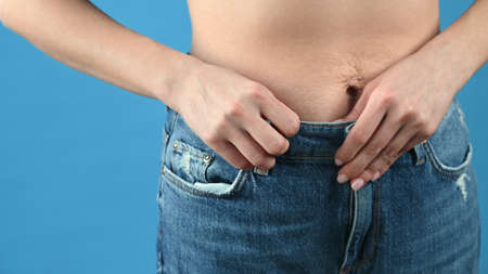 Woman in jeans show off the belly after birth and weight loss. Stretch marks on blue background with copy space. High quality photoの写真素材