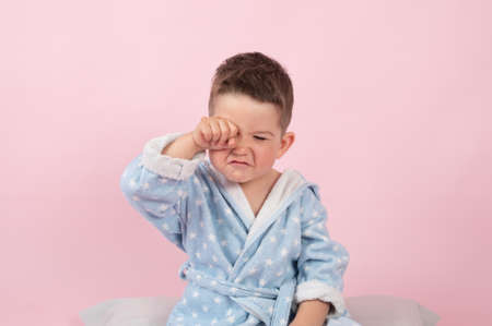 Cranky child boy refuses to go to bed. Kid boy in bathrobe on pink background. High quality photoの写真素材