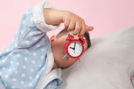 Little boy with a red alarm clock in his hands. Morning concept. Children's sleep. High quality photoの写真素材
