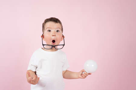 Surprised little boy holds a light bulb in his hand on pink background. Idea concept. High quality photoの写真素材