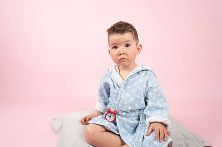 Little boy with a red alarm clock on pink background. Morning concept. Childrens sleepの写真素材