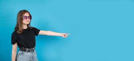 The teen girl in black t-shirt points her hands to the side on blue background, banner. High quality photoの写真素材