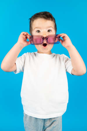 Kid boy in white t-shirt wearing violet glasses. Cheerful little boy in sunglasses express surprised face. High quality photoの写真素材