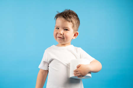 A little boy gently holds in his hand roll of toilet paper on blue background. The buying toilet paper concept. High quality photoの写真素材