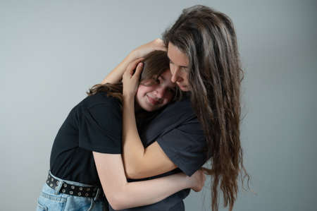 Concept of family support and trust. Mom hugs and comforts teenage daughter on gray background. High quality photoの写真素材