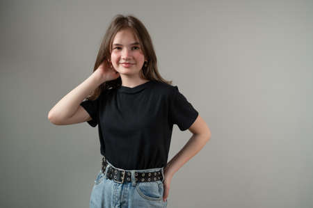 Smiling brunette teen girl in black t-shirt straightens her hair on gray backgroundの写真素材