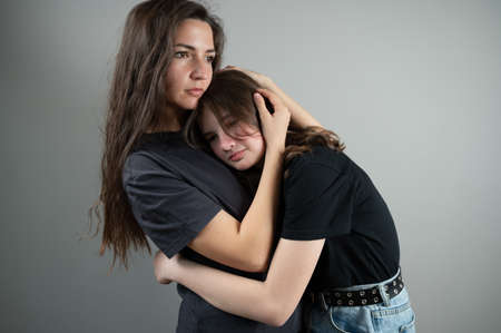Concept of family support and trust. Mom hugs and comforts teenage daughter on gray backgroundの写真素材