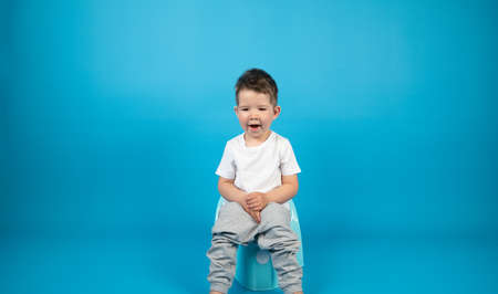 Full-length portrait of a yawning toddler sitting on a potty, blue background with copy space. High quality photoの写真素材