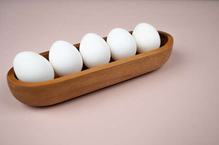 White eggs in a wooden plate on a pink background. Organic eggs and healthy nutrition concept