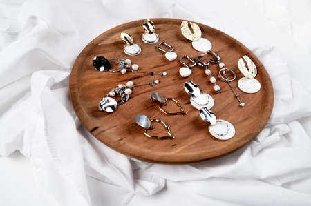 Jewelry on a wooden podium. Set of stylish silver and gold earrings with pendants and pearls. High...