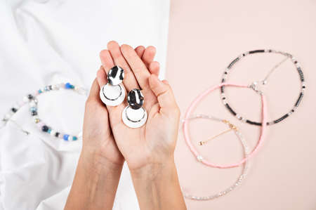 Pair of stylish earrings with round white pendants in woman hand on pink backgruond. Women's jewelry. High quality photoの写真素材