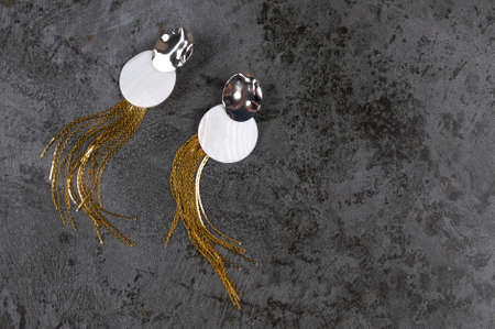 Pair of stylish silver-gold earrings with natural nacre pendants on gary concrete background.