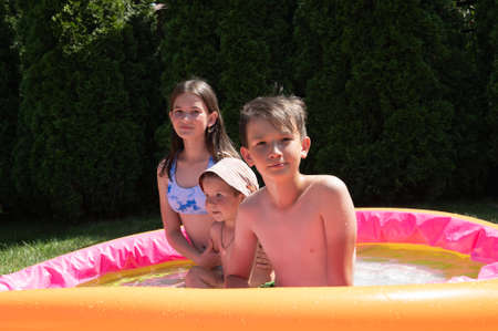 Two teenagers have fun in an inflatable pool with their younger brother. High quality photo