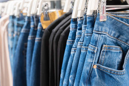 Denim jeans store detail. Row of blue jeans hung on plastic hangers in store. Many jeans are hanging on counter. High quality photoの写真素材