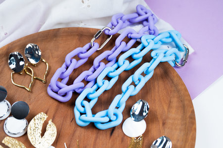 Women's jewelry. Stylish women's earrings and two multicolored chokers plastic choker on wooden display, white crumpled fabric background. High quality photoの写真素材