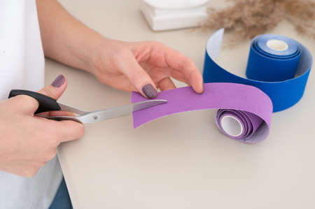 Female cosmetician cuts kinesio tape for non-invasive lifting treatment. Recovery, anti-aging...