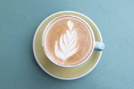 A cup of cappuccino with latte art on blue background. Beautiful foam, top viewの写真素材