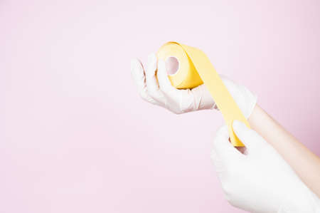 The beautician in protective gloves holds tapes in her hands on pink background. anti-aging...