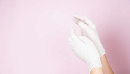 Tender female hands in white disposable gloves on pink background with copy space. Cosmetology and medicine concept.の写真素材