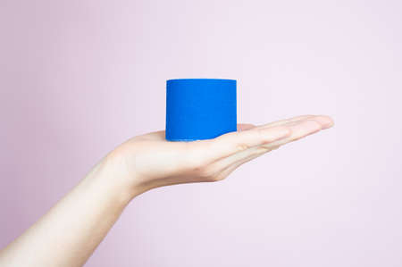 Blue tape roll in her hand on pink background, close up. Anti-aging procedures, skin and body care.