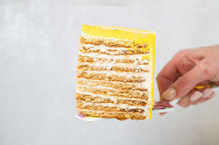 Woman holding honey cake covered with yellow icing. Layered honey cake. Closeup viewの写真素材