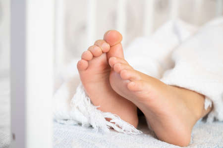 Childrens legs stick out from under the blanket. Close up of a childrens feet, copy spaceの写真素材