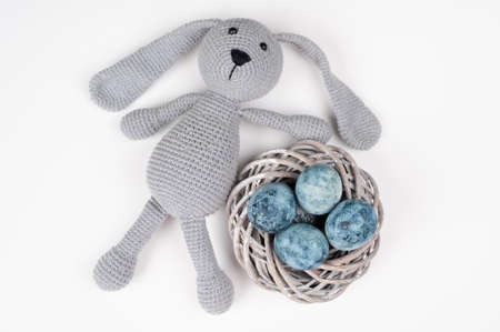 Easter knitted bunny toy and nest with eggs on white background. Space for text