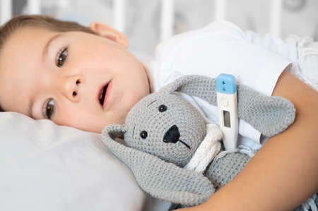 The little boy is sick in bed with a thermometer and high temperature. high quality photoの写真素材