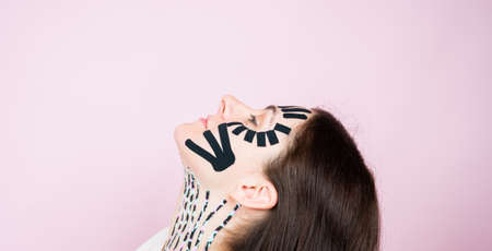 Portrait of woman with colorful tapes on face and neck on pink surface. face aesthetic taping. Lifting skin concept.の写真素材