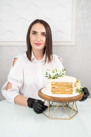 Pastry chef holding delicious wedding cake with floral decoration. Cut cake with visible layers.