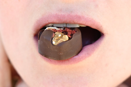 A chocolate candy in the mouth close up. Woman eating chocolate, holding candy in mouthの写真素材