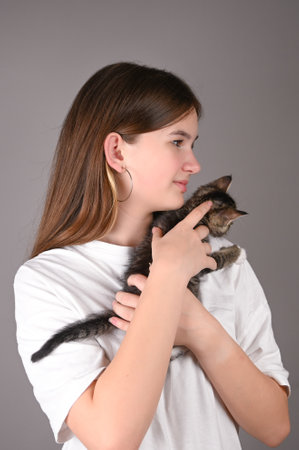 Teen girl holding a baby cat on gray background. Portrait of young girl with kitten. Kids and pets.の写真素材