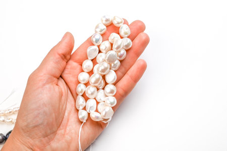 Close-Up of woman hand with string of white baroque pearls isolated on white. Cropped hand holding...
