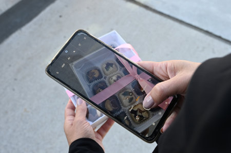 Female hand holding smartphone and taking photo of chocolate box