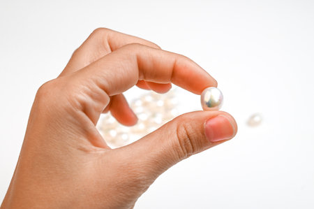 Close up of woman hand holding white pearl. A woman determines the size, shape, color, surface quality of a natural pearl.の写真素材
