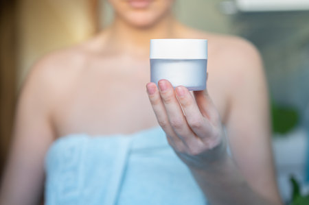 Young woman holding a face cream in her hands. A jar of cream in female hands on blurred abstract background. high quality photoの写真素材