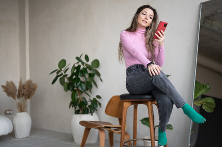 Nice attractive focused girl sitting on a wooden stool holding in hands digital device gadget spending free timeの写真素材