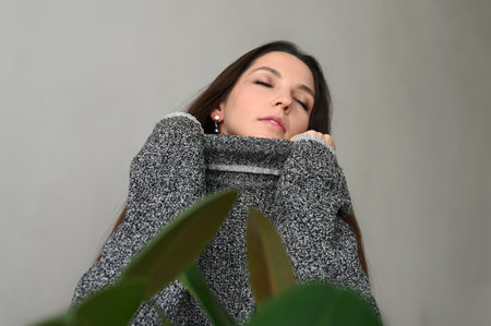 Close-up of beautiful brunette woman pulling sweater on face, standing over concrete background....