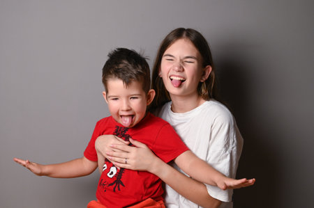 Brother and sister fooling around on gray background. Close up portrait of a happy little brother and teen sisterの写真素材