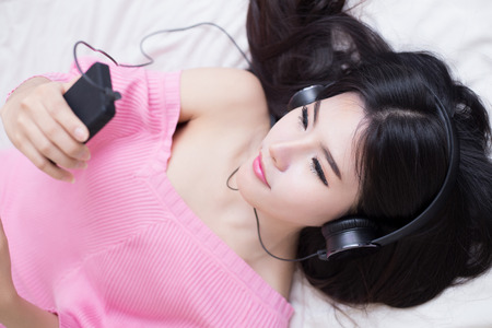 young woman listening music in headphones on her bedの写真素材