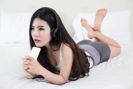 young woman listening music in headphones on her bedの写真素材