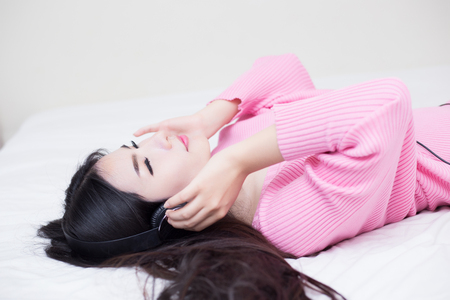 young woman listening music in headphones on her bedの写真素材