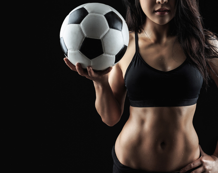 Beautiful body of fitness model holding soccer ball isolated on black backgroundの写真素材